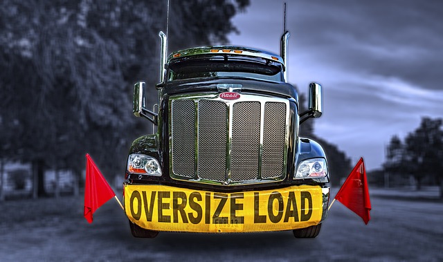 Front view of a large truck with an "Oversize Load" sign and red flags on a rural road
