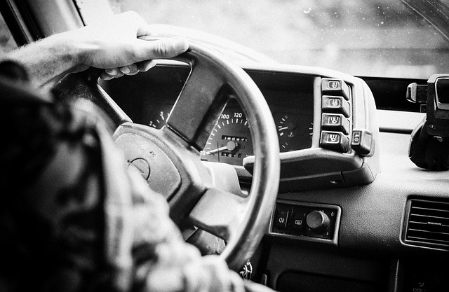 Driver's hands on steering wheel of a car, black and white dashboard and speedometer in view