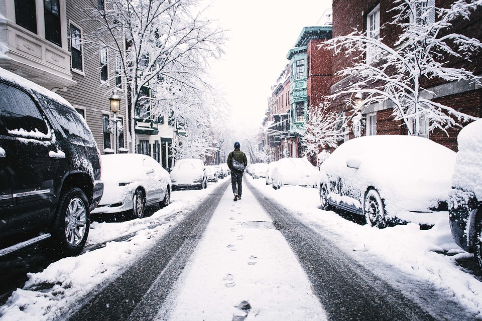 Person walking down a snowy city street with parked cars covered in snow